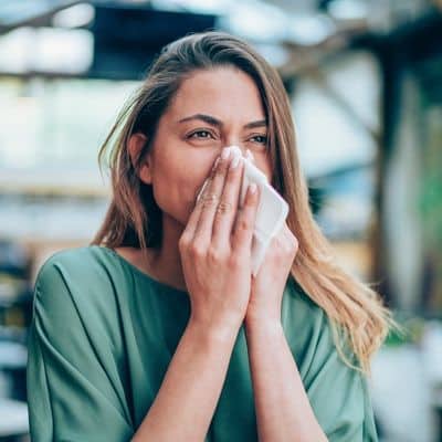 woman outdoors holding tissue to nose