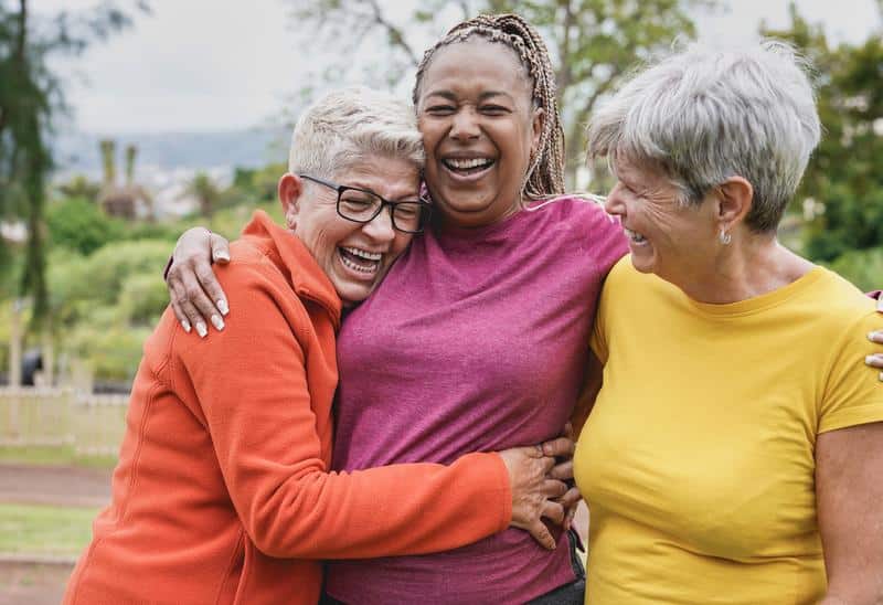 happy and healthy senior women laughing outside and hugging